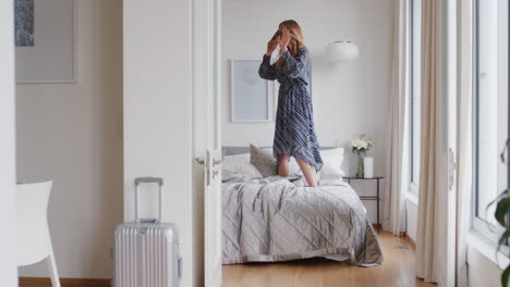 happy woman jumping on bed in hotel room having fun enjoying vacation lifestyle celebrating freedom