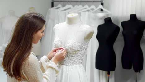 Portrait-of-a-girl-creating-a-wedding-dress-by-exclusive-order-sewing-fabrics-and-rhinestones-on-a-dress-dressed-in-a-mannequin.-production-of-wedding-dresses.-Little-business