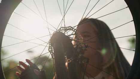 joven adulto tocando suavemente la rueda de la bicicleta mientras la luz del sol se refleja en ella, creando un efecto de ensueño, la rueda gira suavemente mientras ella la admira, con un fondo borroso de vegetación
