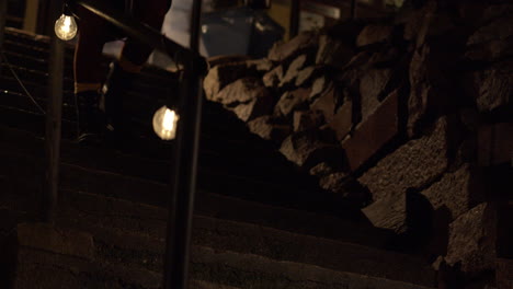 Medium-wide-shot-of-a-person-walking-down-steps-at-nighttime,-with-festoon-lighting