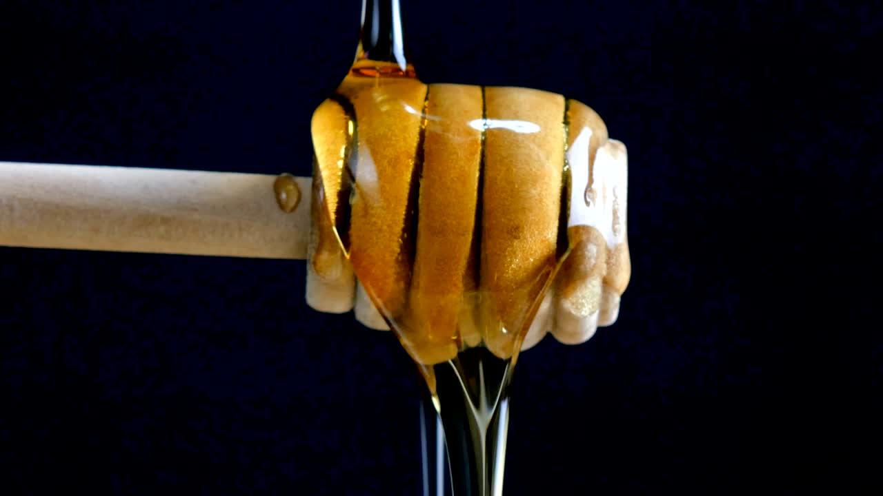Pouring honey to dripper stick againt black blackground