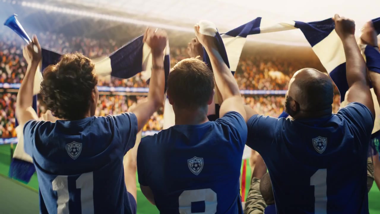 Close-up de torcedores de futebol felizes levantando cachecóis em estádio lotado.