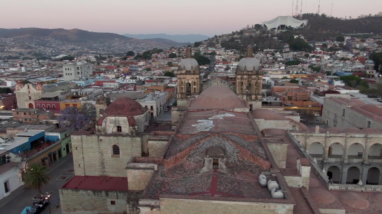 Ripresa aerea con drone di un complesso di cattedrali storiche con cupole, torri, cortili e architettura in pietra invecchiata, circondato da fitti quartieri urbani a Oaxaca, Messico.