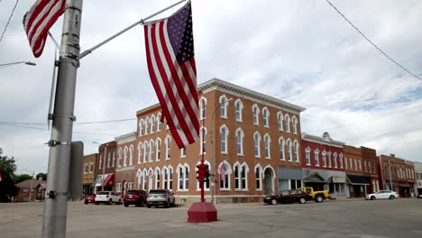 Antiguo-Semáforo-De-Cuatro-Vías-Y-Bandera-Estadounidense-En-El-Centro-De-Toledo,-Iowa,-Con-Vídeo-Estable-De-Cerca-En-ángulo