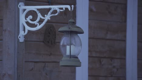 retro metal lantern with a candle inside, hanging from a wooden house and swinging in the wind, at night