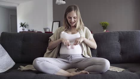 happy pregnant woman playing with babys bootees on her belly