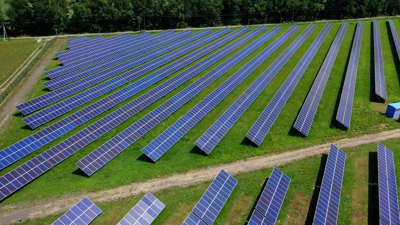 Power energy solar farm in the countryside. Photovoltaic solar batteries near the forest in bright summer day. Alternative source of clean energy. Aerial view