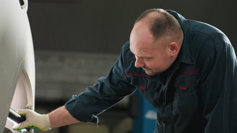 mechanic in blue uniform using torchlight to inspect car tire in auto repair shop, focusing closely with blue lift in background, ensuring safety and maintenance in professional automotive workshop