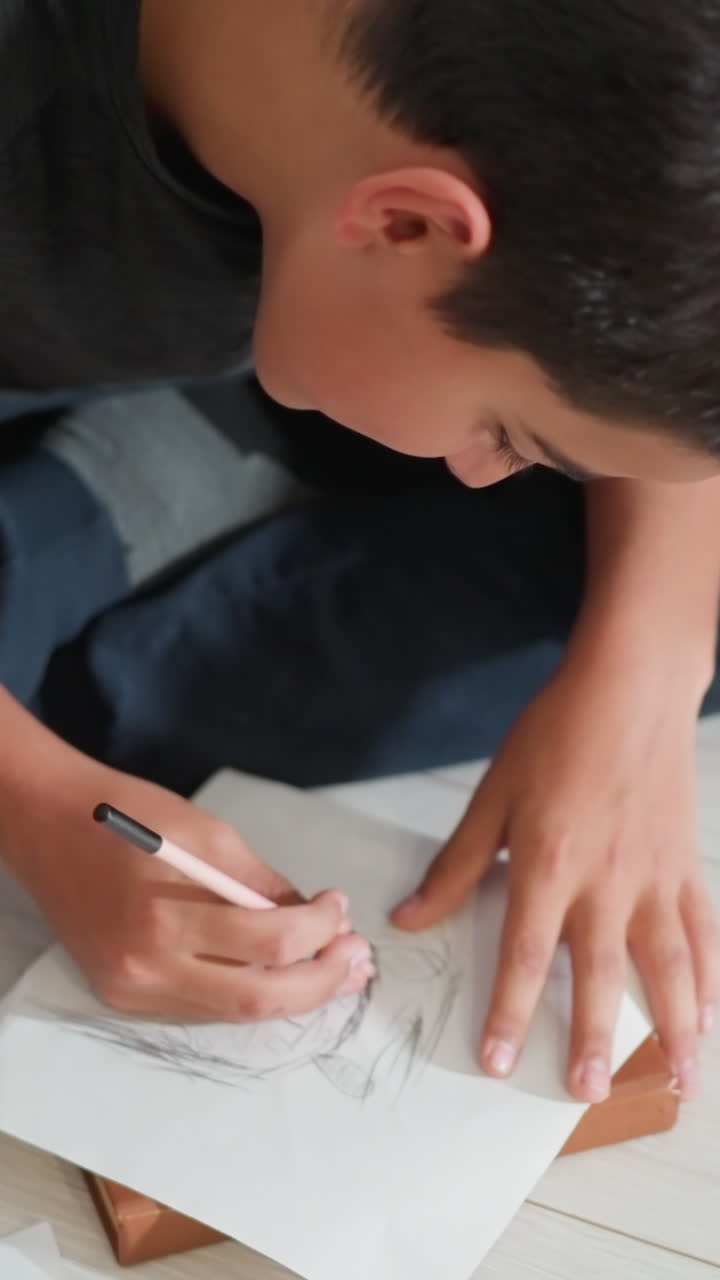Niño pequeño sentado con las piernas cruzadas en el suelo, muy concentrado en dibujar un retrato a lápiz durante un momento creativo y tranquilo cerca del sofá, capturando el aprendizaje artístico temprano y la imaginación en un entorno hogareño natural.