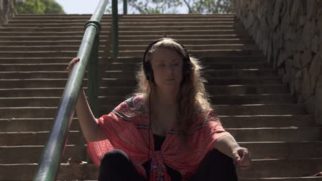 carefree blonde woman listening to music in headphones in the park