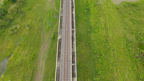 reverse aerial footage of an elevated railroad, grassland both left and right, saraburi, thailand