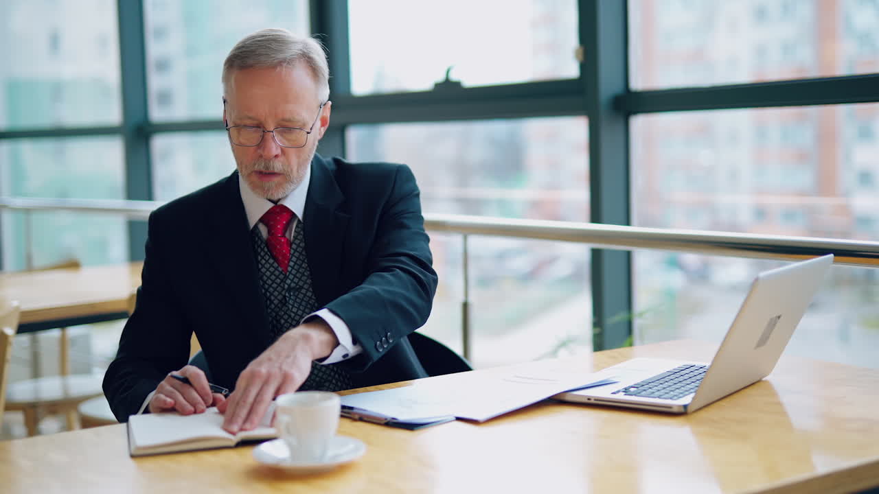 Smart mature businessman working in the office. Senior man in elegant suit sitting at the desk and using notebook in his work. Business concept.