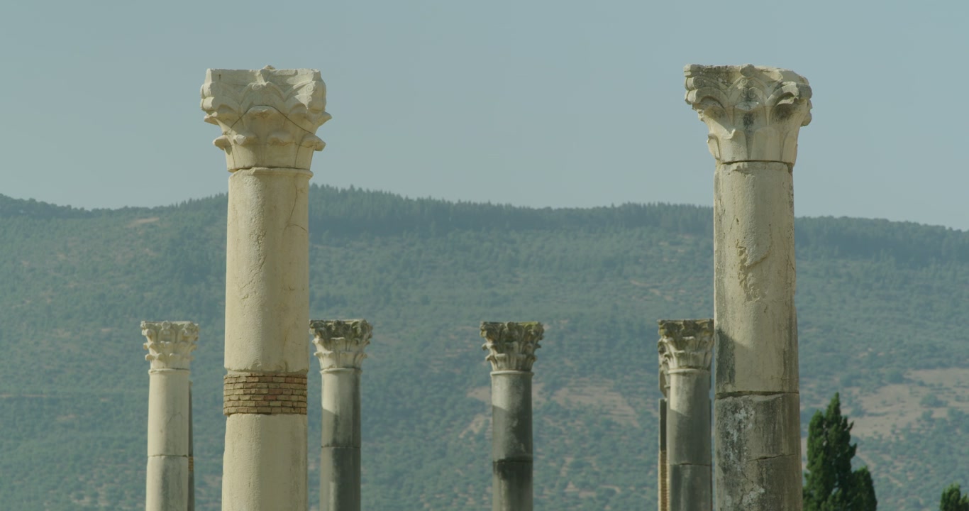 Vista cinematografica a livello del suolo delle colonne corinzie del Campidoglio nel sito archeologico di Volubilis, patrimonio UNESCO, che mostra l'architettura monumentale del principale tempio romano nell'antica.