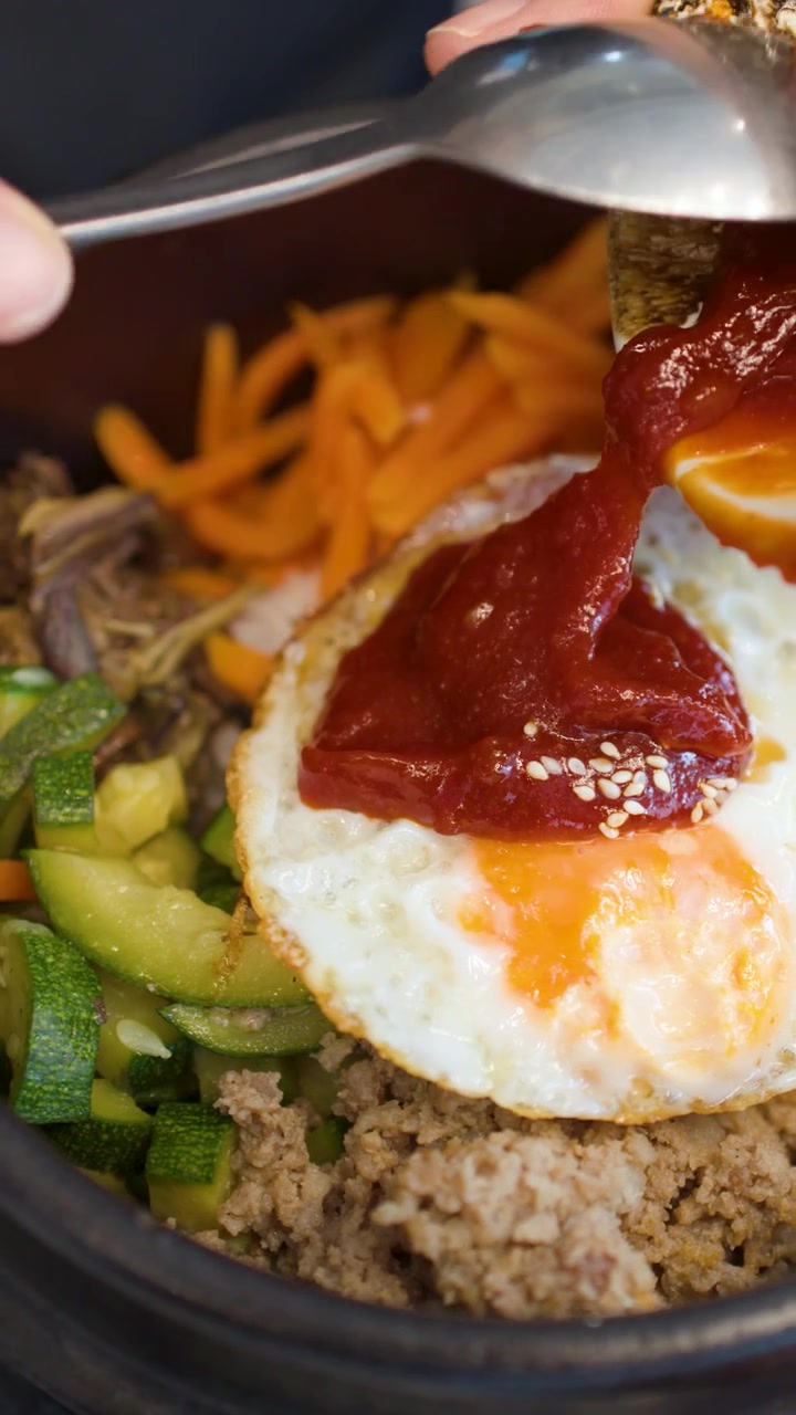 Bidikan jarak dekat pasta cabai merah sedang disendokkan ke atas mangkuk batu bibimbap
