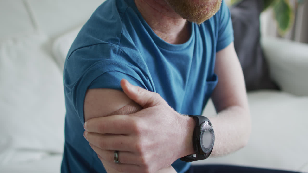 Uomo afroamericano albino felice con un cerotto dopo la vaccinazione seduto sul divano.