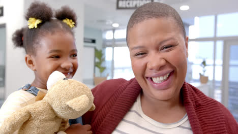 portrait of happy african american mother holding daughter with mascot in hospital, slow motion