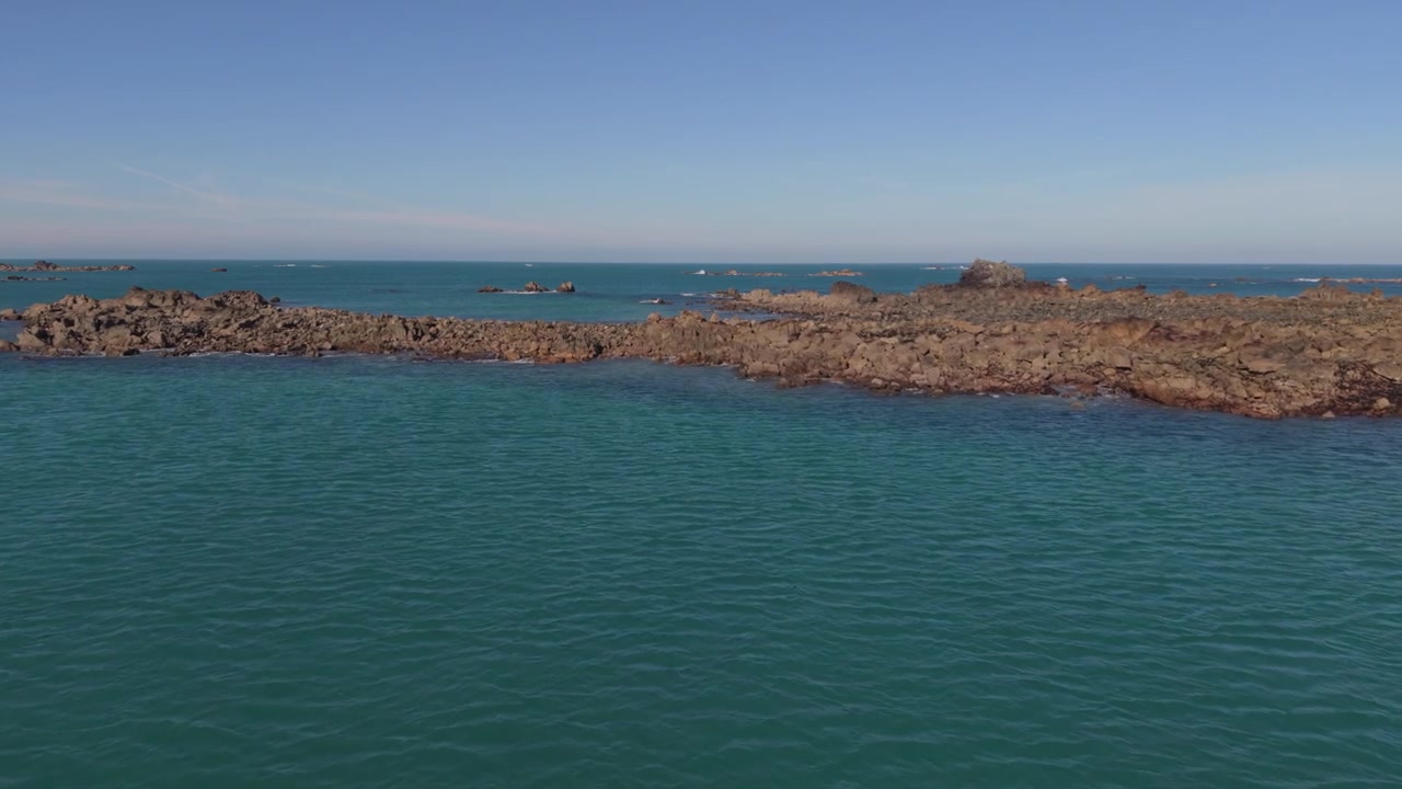 Filmato lento e molto ravvicinato in avanti con drone su formazioni rocciose in mare aperto al sole del tardo pomeriggio con mare calmo e limpido, cielo blu e viste su affioramenti rocciosi distanti all'orizzonte