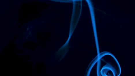 video of a white smoke on a black background backlit with blue light. close up. slow motion