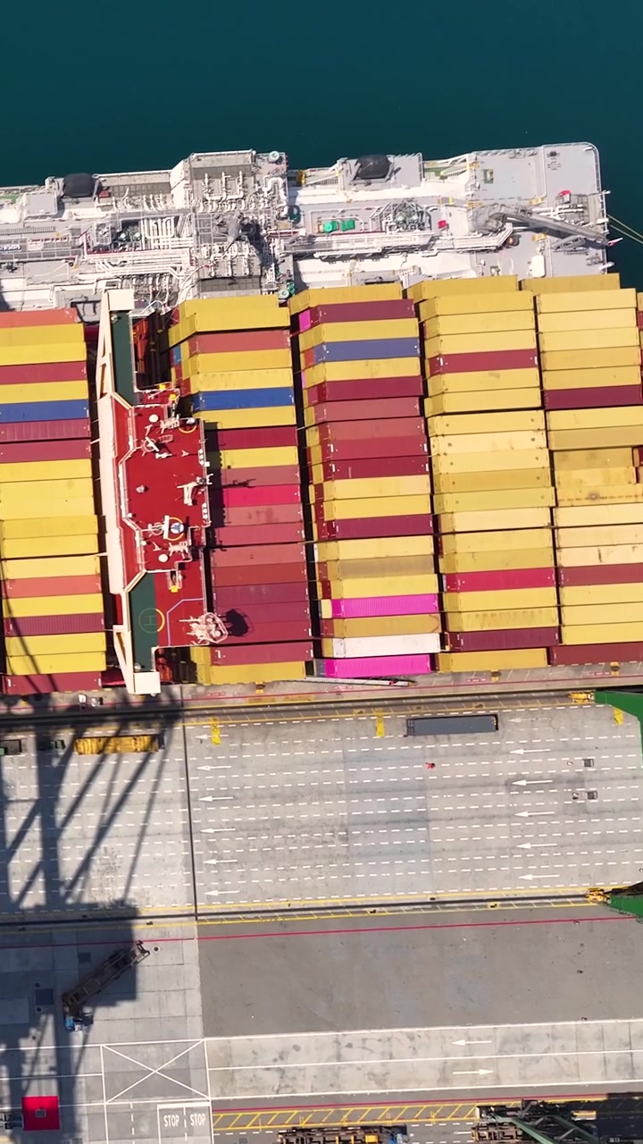 Container terminal shows multiple shipping containers stacked in organized rows near the water. Cargo ships are loading and unloading, facilitating international trade.