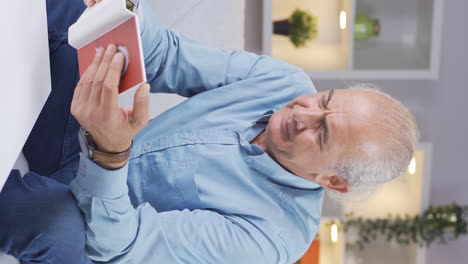 Vertical-video-of-Old-man-looking-at-family-album-with-trembling-hand.