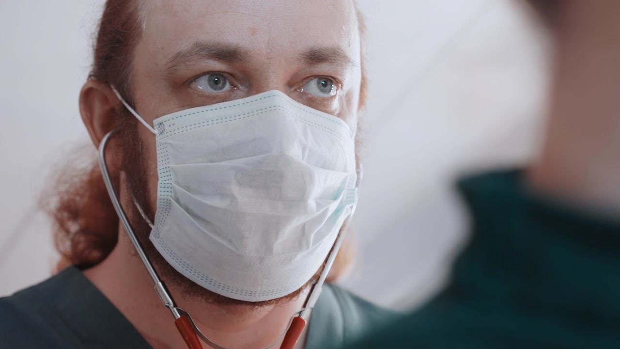 Professionista medico con mascherina valuta attentamente il paziente. Operatore sanitario maschio con mascherina e abbigliamento protettivo esegue una valutazione approfondita del paziente con attenzione e precisione