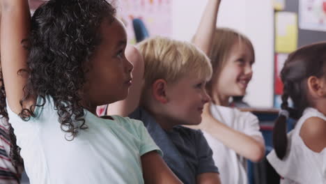 group of elementary school pupils sitting on floor raising hands to answer question