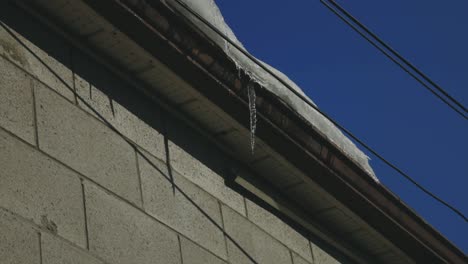 Eiszapfen,-Der-Auf-Die-Dachrinne-Eines-Hausdachs-Gegen-Den-Blauen-Himmel-Tropft