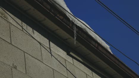 icicle dripping on gutter of a house roof against blue sky