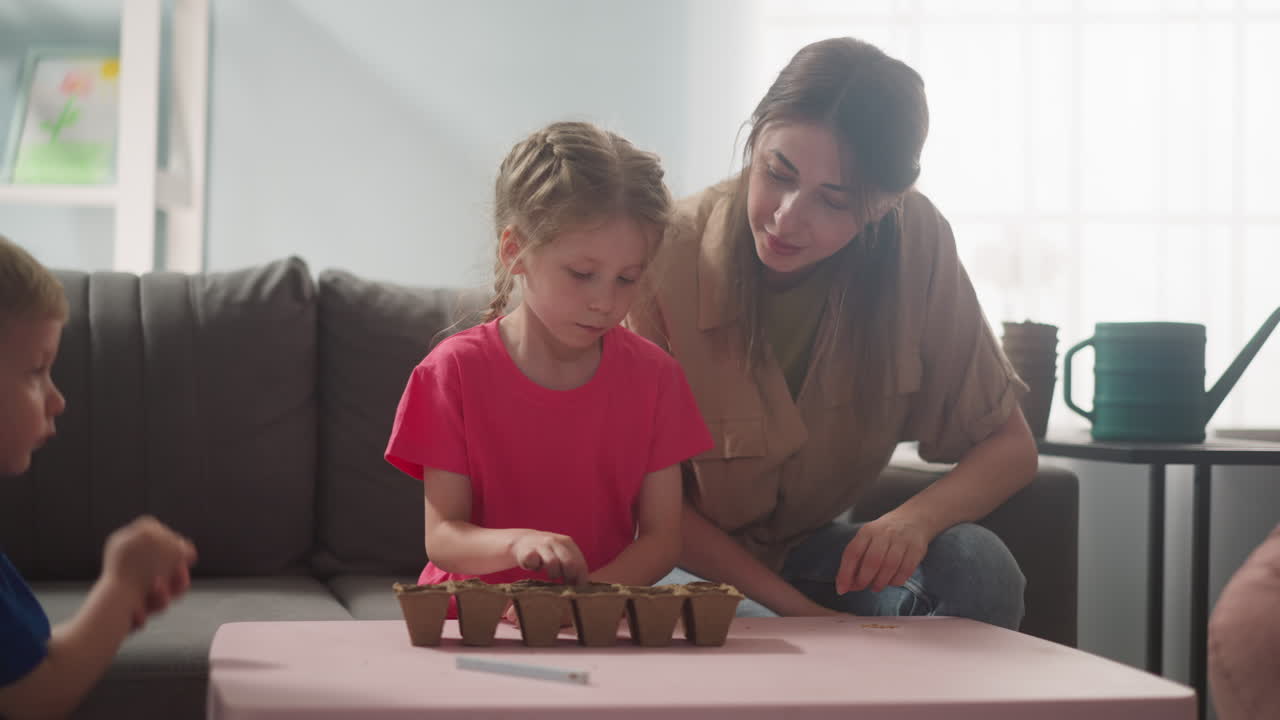 la niña pone semillas en la bandeja de semillas con la madre y el hermano