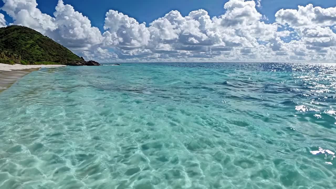 Luftaufnahme von einem ruhigen Strand mit türkisfarbenem Wasser und üppigen Hügeln unter einem bewölkten Himmel