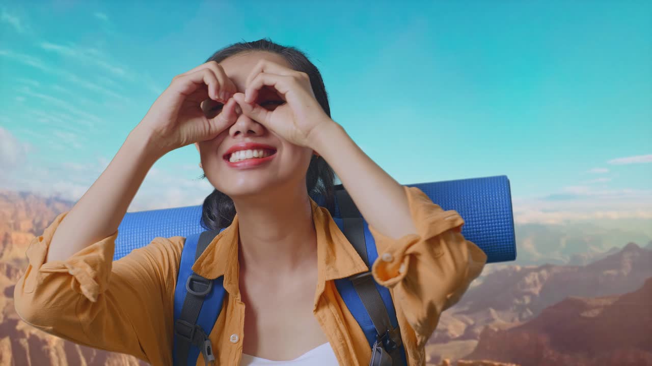 Close Up Of Asian Female Hiker With Mountaineering Backpack Smiling And Making Binoculars Gesture Then Looking Around While Traveling At The Top Of Mountain