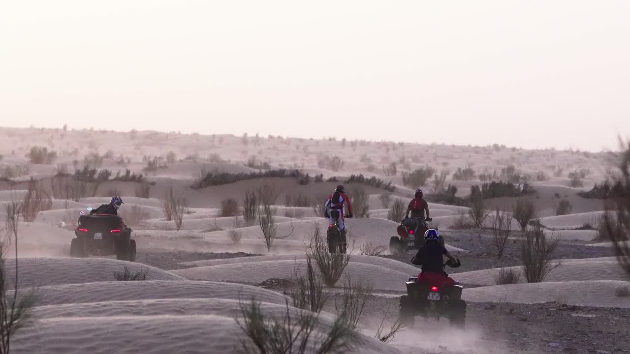 Gruppo di motociclisti su ATV e moto da cross che attraversano il paesaggio desertico tunisino attraverso dune di sabbia e polvere durante un'avventura all'ora d'oro in un ambiente selvaggio fuoristrada con terreno naturale