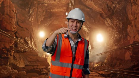 angry asian male engineer with safety helmet shouting at someone while standing in underground mine tunnel