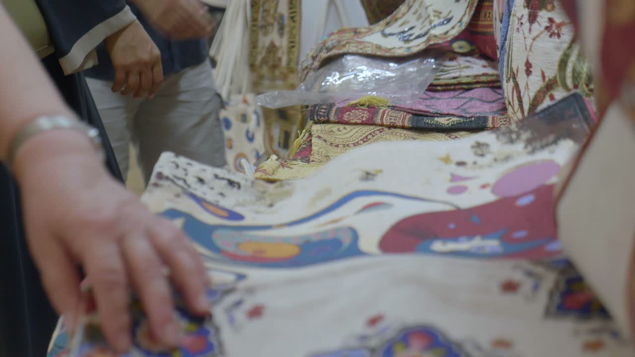 People examining patterned fabrics at a market stall