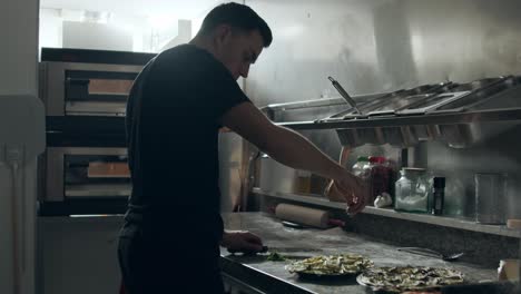 Pizza-maker-spreading-parsley-over-pizza-in-kitchen