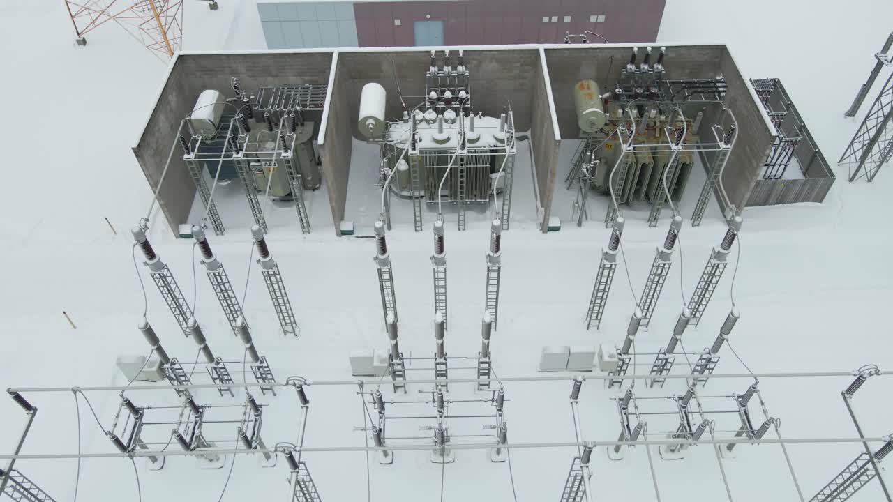 Top down start pulls back to unveil transformers, insulators, and pylons across a frost covered electrical switchyard
