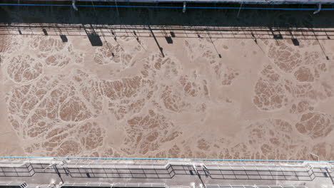 a zoomed-in aerial shot of one aeration basin at the spokane facility shows swirling tan foam textures with a pedestrian walkway and railing overhead