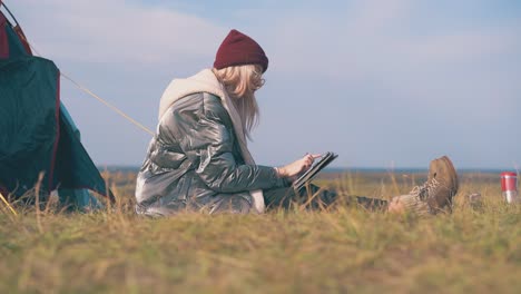 Blonde-Dame-In-Jacke-Mit-Tablet-Im-Zelt-Auf-Trockenem-Gras