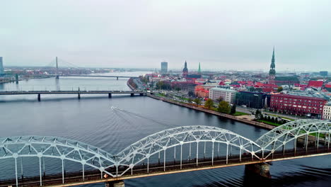 Aerial-view-of-Daugava-river,-rail-bridge-alongside-Riga-City-in-Latvia-on-a-cloudy-daytime