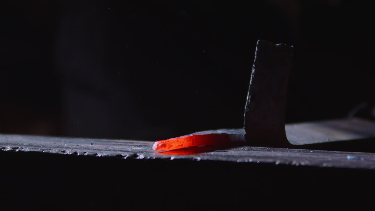 Clanging hammer blows by blacksmith on glowing hot piece of iron on anvil, moody