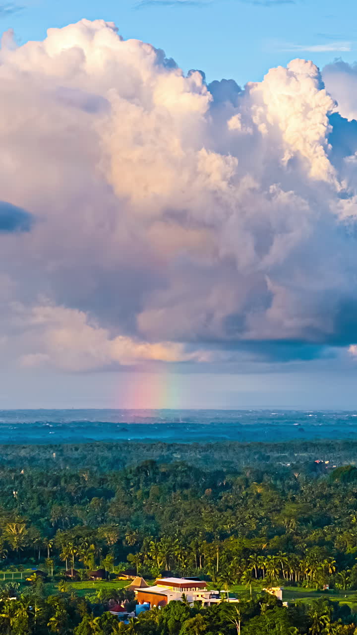 Puffy clouds over Bali landscape with faint rainbow appear on horizon, aerial hyperlapse