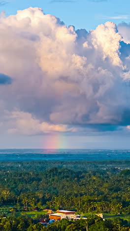 puffy clouds over bali landscape with faint rainbow appear on horizon, aerial hyperlapse