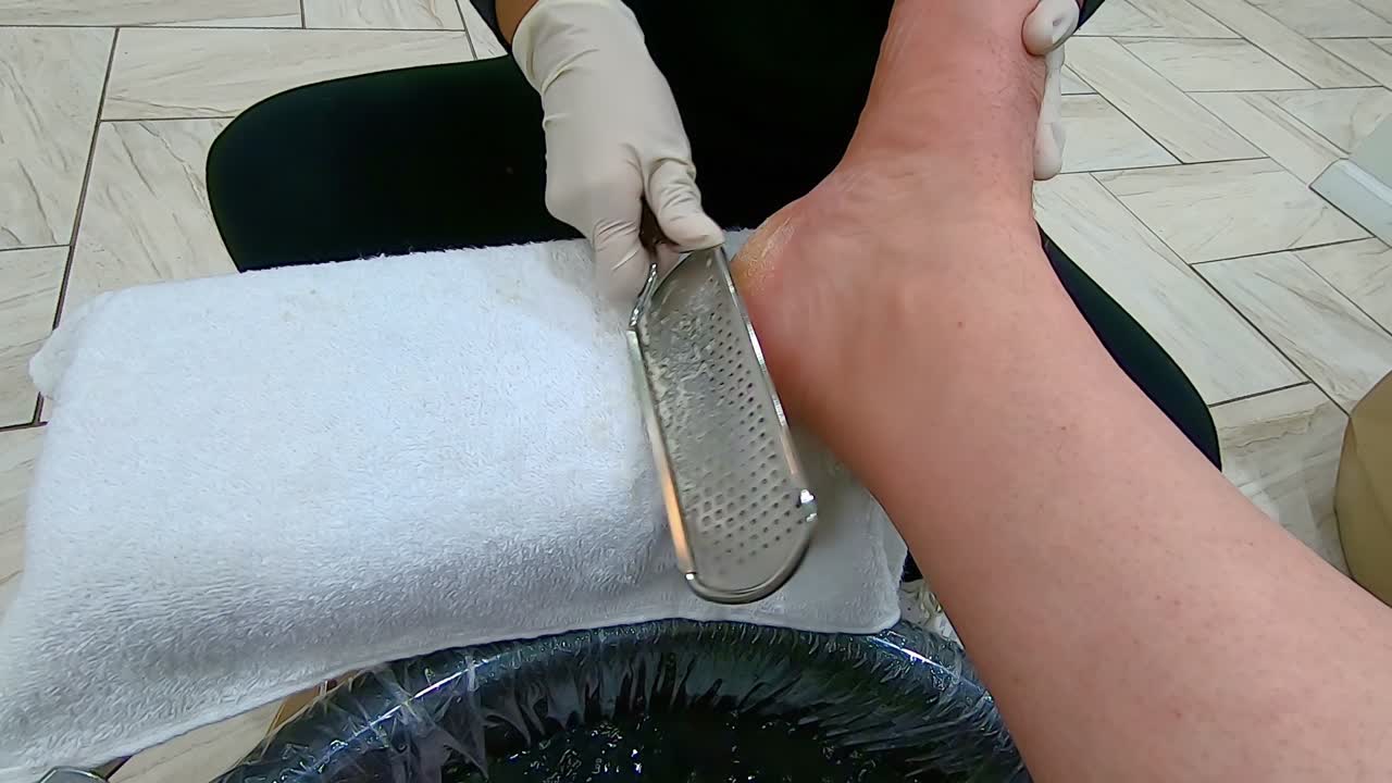 Pedicurista professionista rimuove i calli dal tallone destro di un uomo usando un levacalli o una raspa.