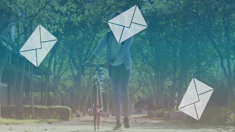 animation of falling envelope icons over biracial woman wearing mask walking with bicycle in park