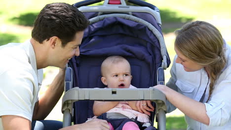 Glückliche-Eltern-Neigen-Zu-Babymädchen-Im-Kinderwagen-Im-Park