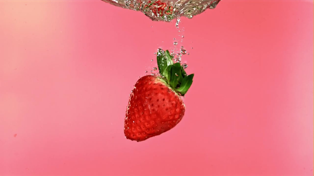 Fresh Strawberry Falling into Water with Splashes and Bubbles on Pink Background