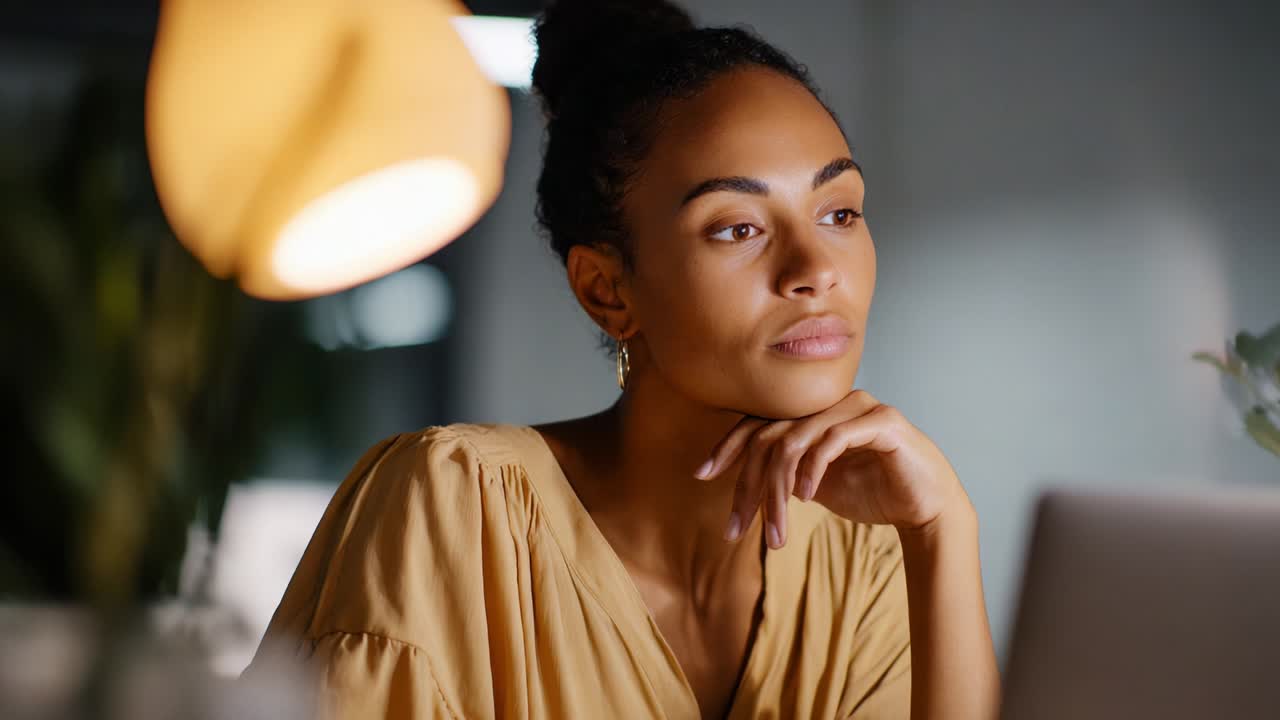 A thoughtful moment captured in a serene and intimate setting, showcasing a young woman in a soft yellow blouse gazing pensively while resting her chin on her hand, illuminated by warm lighting