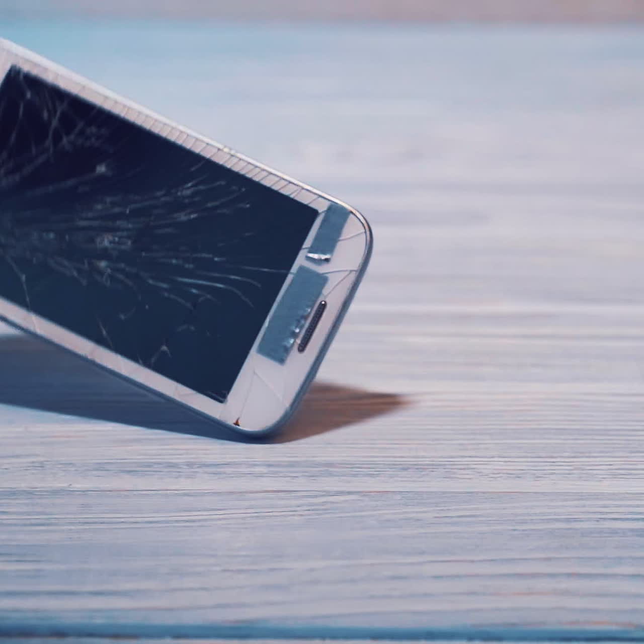Celular touchscreen branco moderno caindo no chão e quebrando, isolado em um piso de madeira. Smartphone quebrado em superfície cinza
