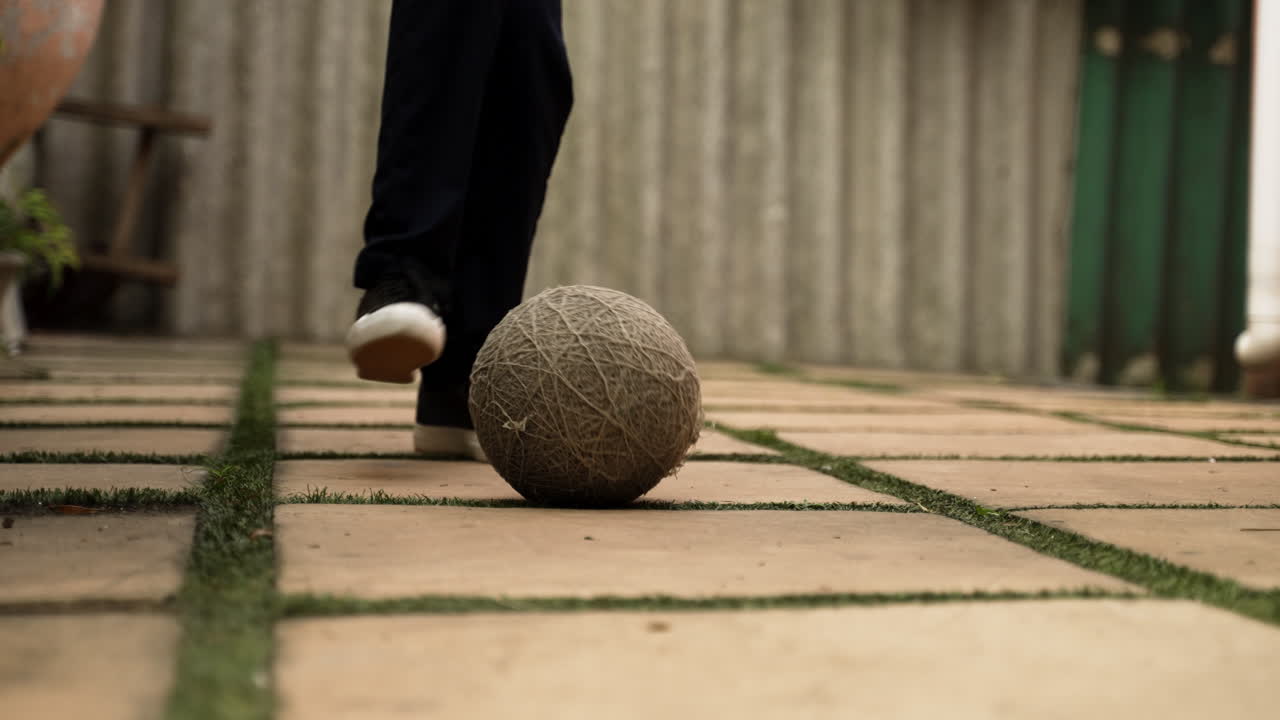 niño jugando en un patio de azulejos con un viejo fútbol