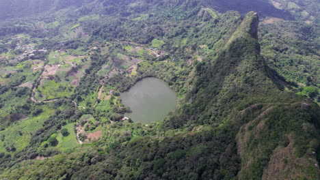 Lago-En-Forma-De-Corazón-Ubicado-Entre-Exuberantes-Colinas-Verdes-Con-Asentamientos-Rurales-Dispersos,-Durante-El-Día,-Vista-Aérea